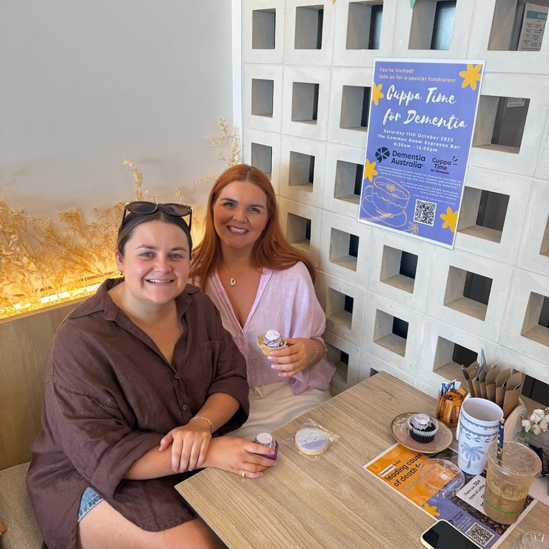 Two friends sitting at a table during a Cuppatime for Dementia event, looking at the camera and smiling.
