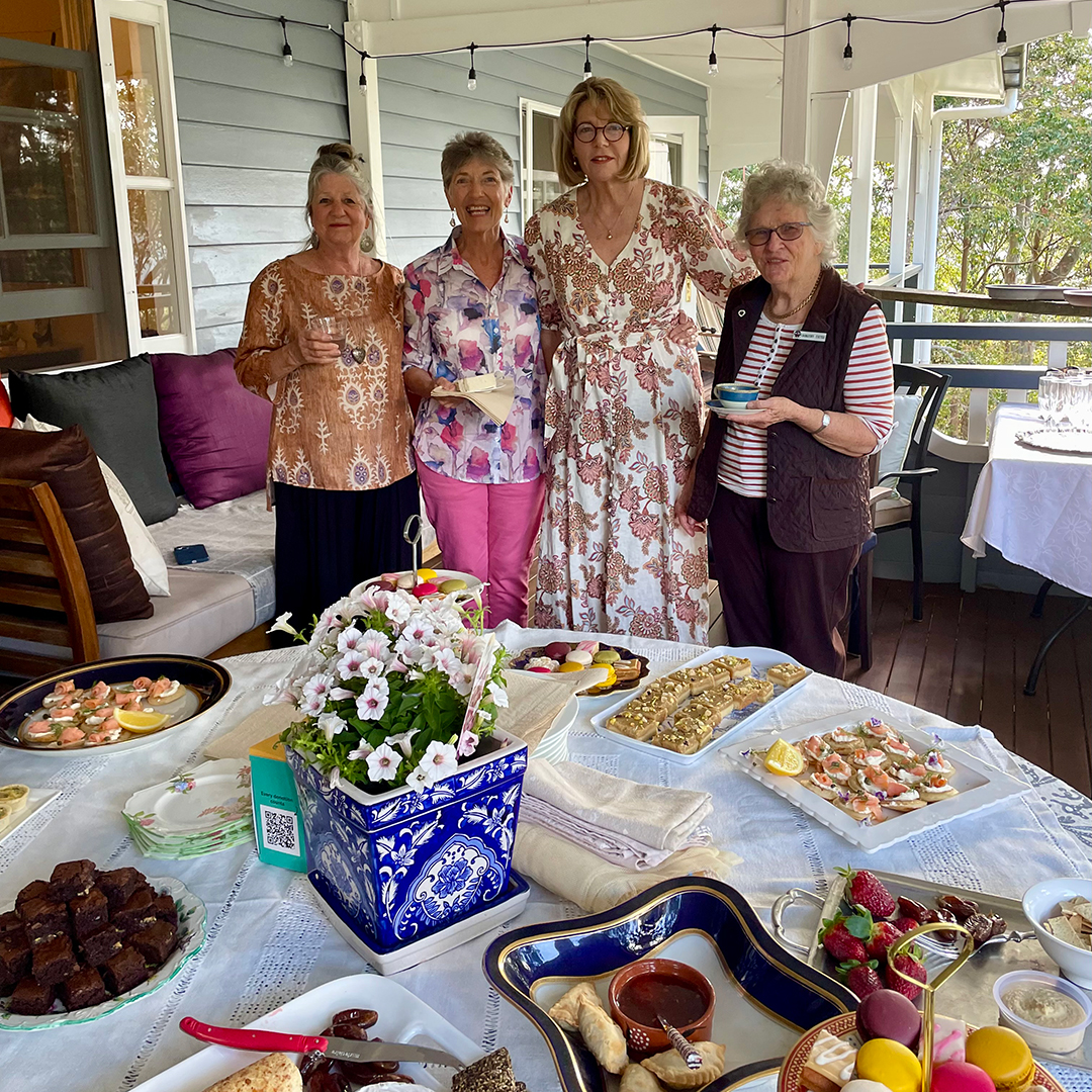 Dorothy and three of her friends standing together outside in front of a table full of food for a Cuppatime for Dementia event.